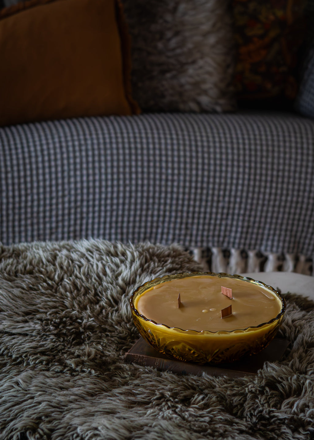 Candle in a Amber Glass Bowl on a textured surface with a blurred sofa in the background