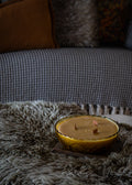 Candle in a Amber Glass Bowl on a textured surface with a blurred sofa in the background