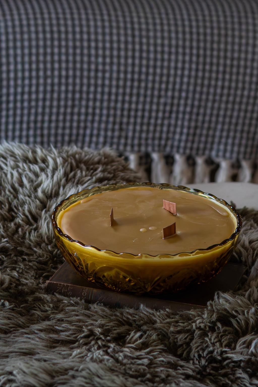 Candle on a textured surface with pillows and a sofa in the background