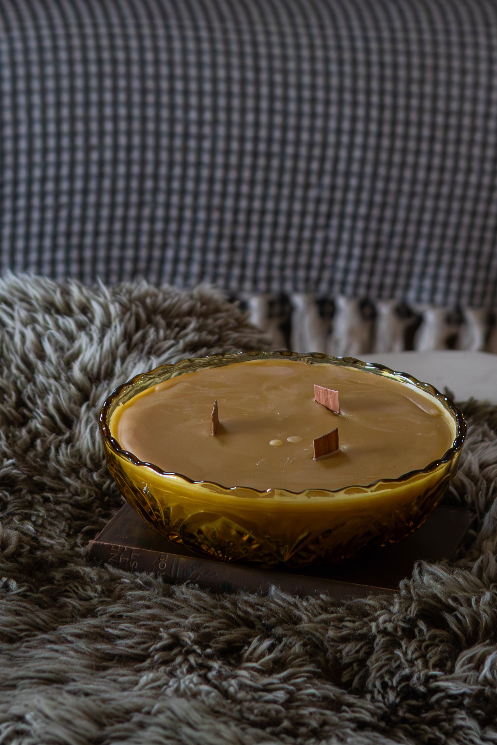 Candle on a textured surface with pillows and a sofa in the background