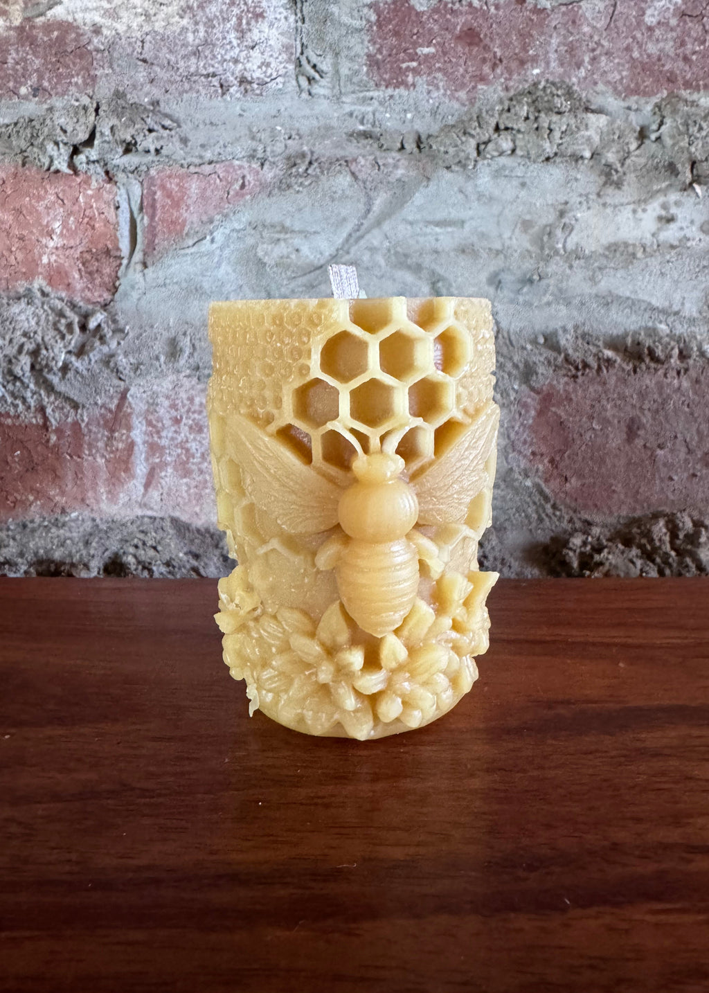 Decorative wooden finial with honeycomb and bee design on a textured wall.
