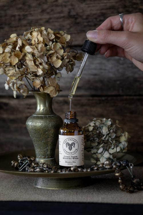 Hand using a dropper to extract oil from a bottle labeled 'Cherry & Sage' with dried flowers and a vase in the background.