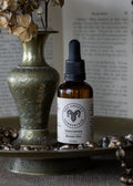 Bottle of Unseated Beard Oil on a decorative tray with dried flowers and an open book in the background.
