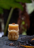 Decorative candle with intricate design on a dark surface with green foliage in the background
