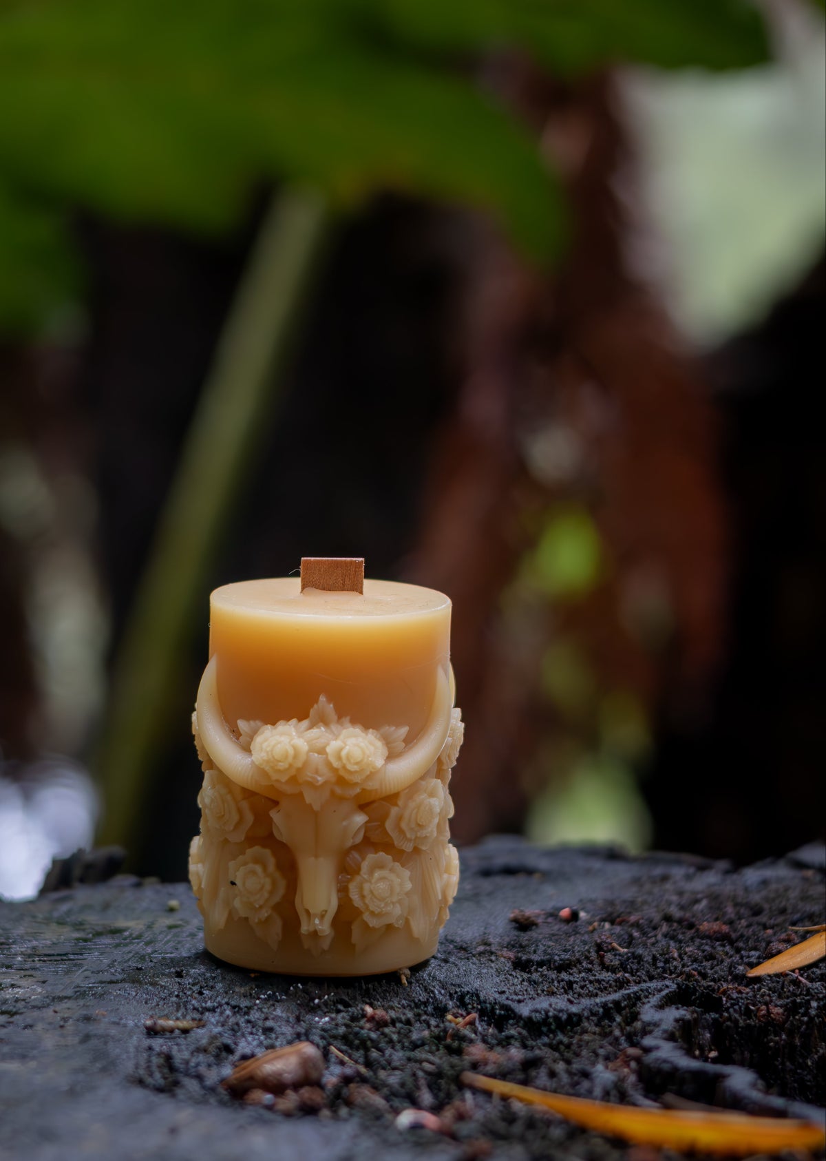Decorative candle with intricate design on a dark surface with green foliage in the background