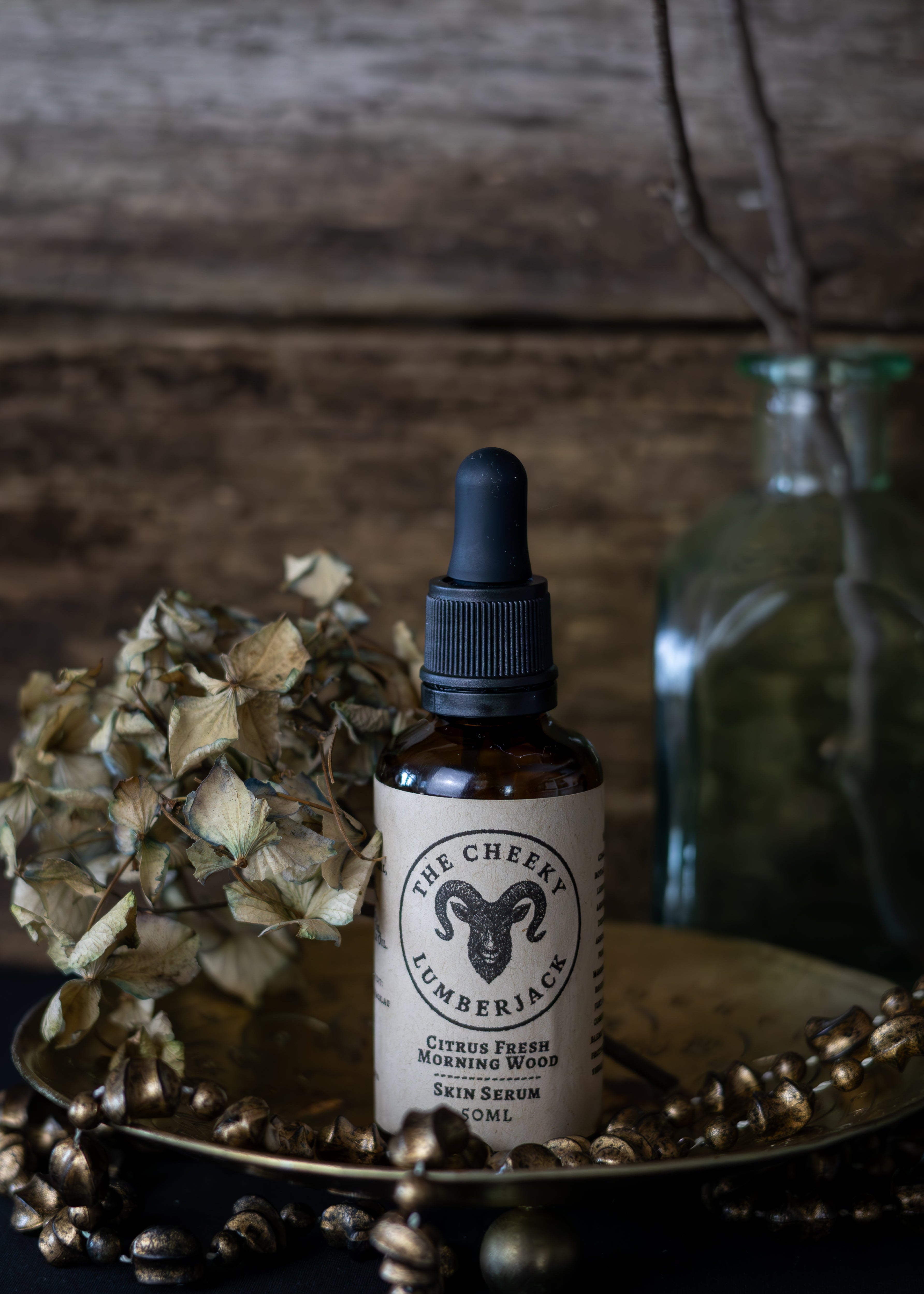 Bottle of 'The Cheeky Lumberjack' skin serum on a wooden surface with decorative elements.