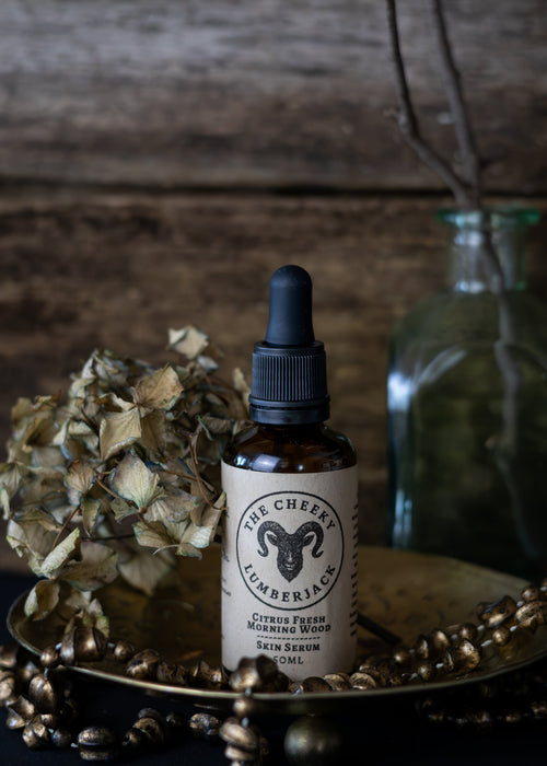 Bottle of 'The Cheeky Lumberjack' skin serum on a wooden surface with decorative elements.