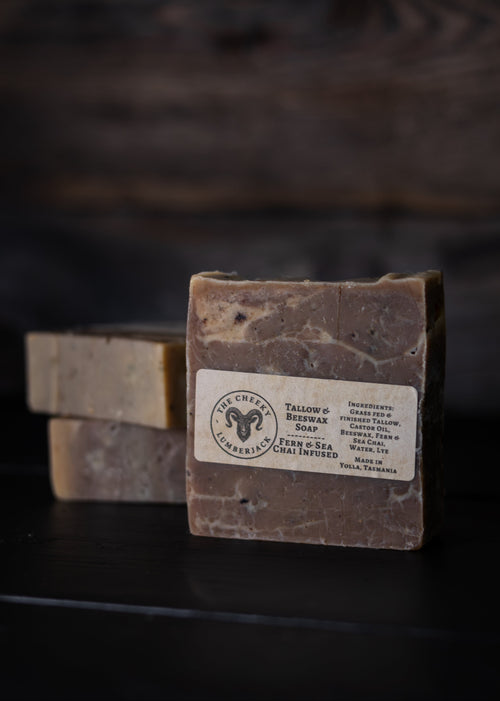 A rectangular bar of soap standing upright on a dark surface, with two additional soap bars blurred in the background. The front bar has a white label reading 'The Creamy Sheep' and 'Tallow & Bee wax Soap'.