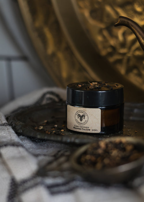 Jar of fern and sea chai  infused tallow with a label on a textured surface