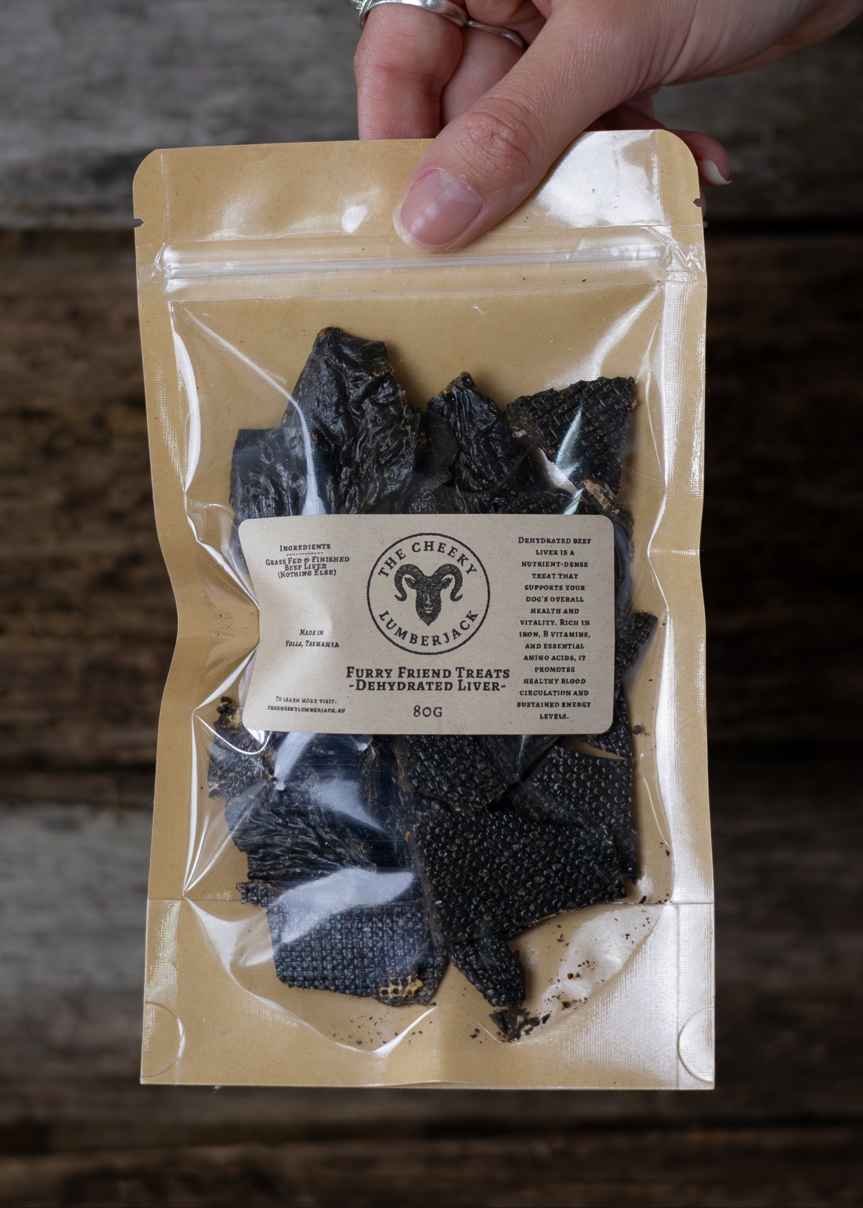 Hand holding a package of dried beef liver with a rustic wooden background
