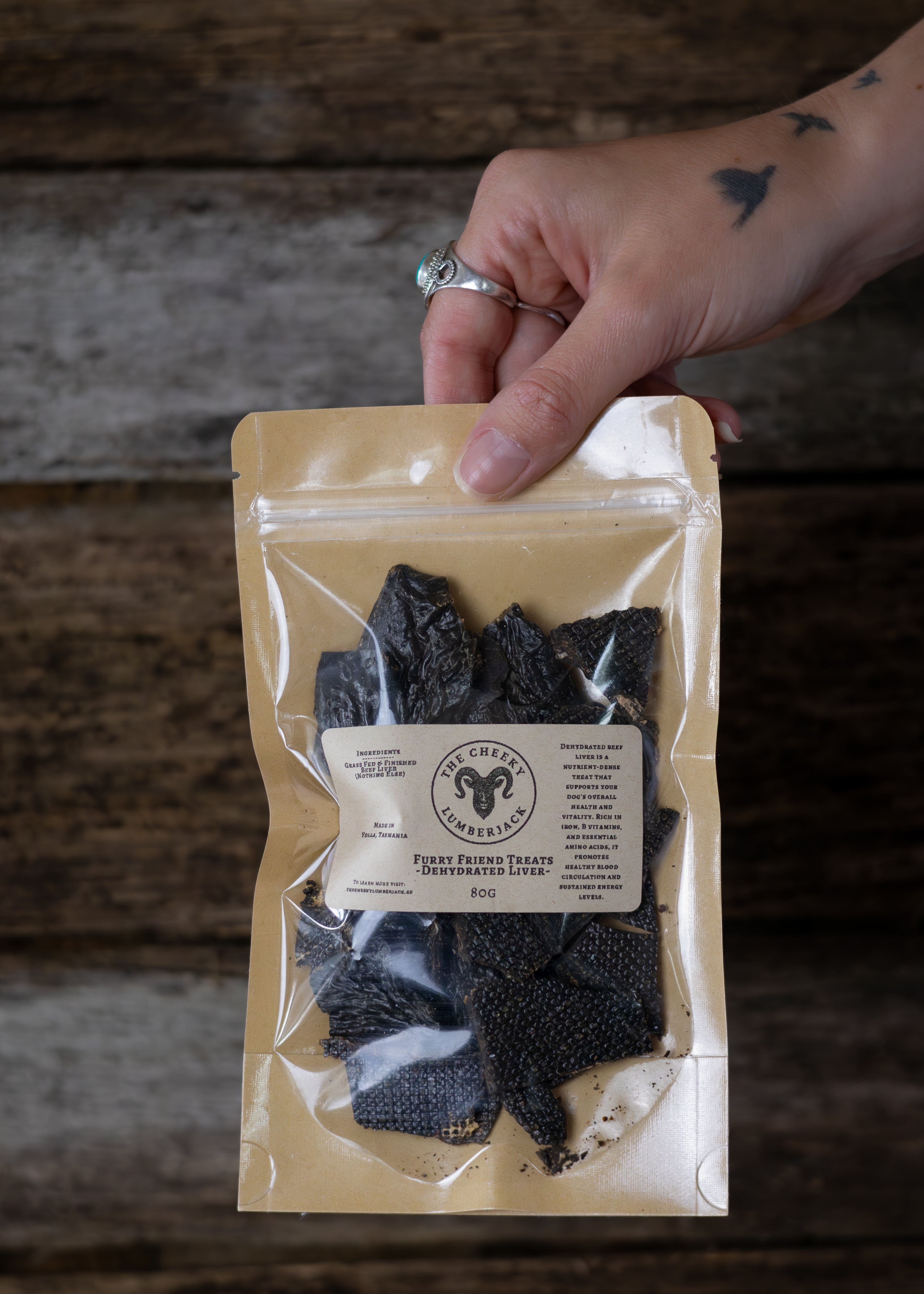 Hand holding a package of dried beef liver with a rustic wooden background