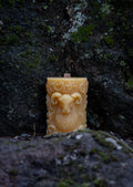 Beeswax candle with a face design on a mossy stone surface