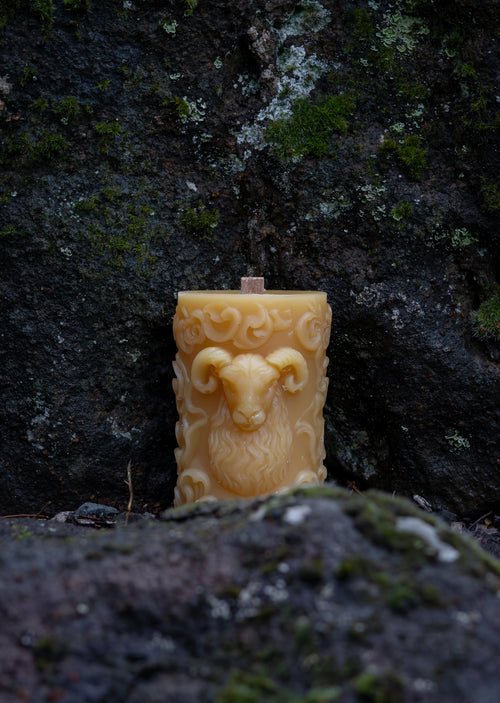 Beeswax candle with a face design on a mossy stone surface