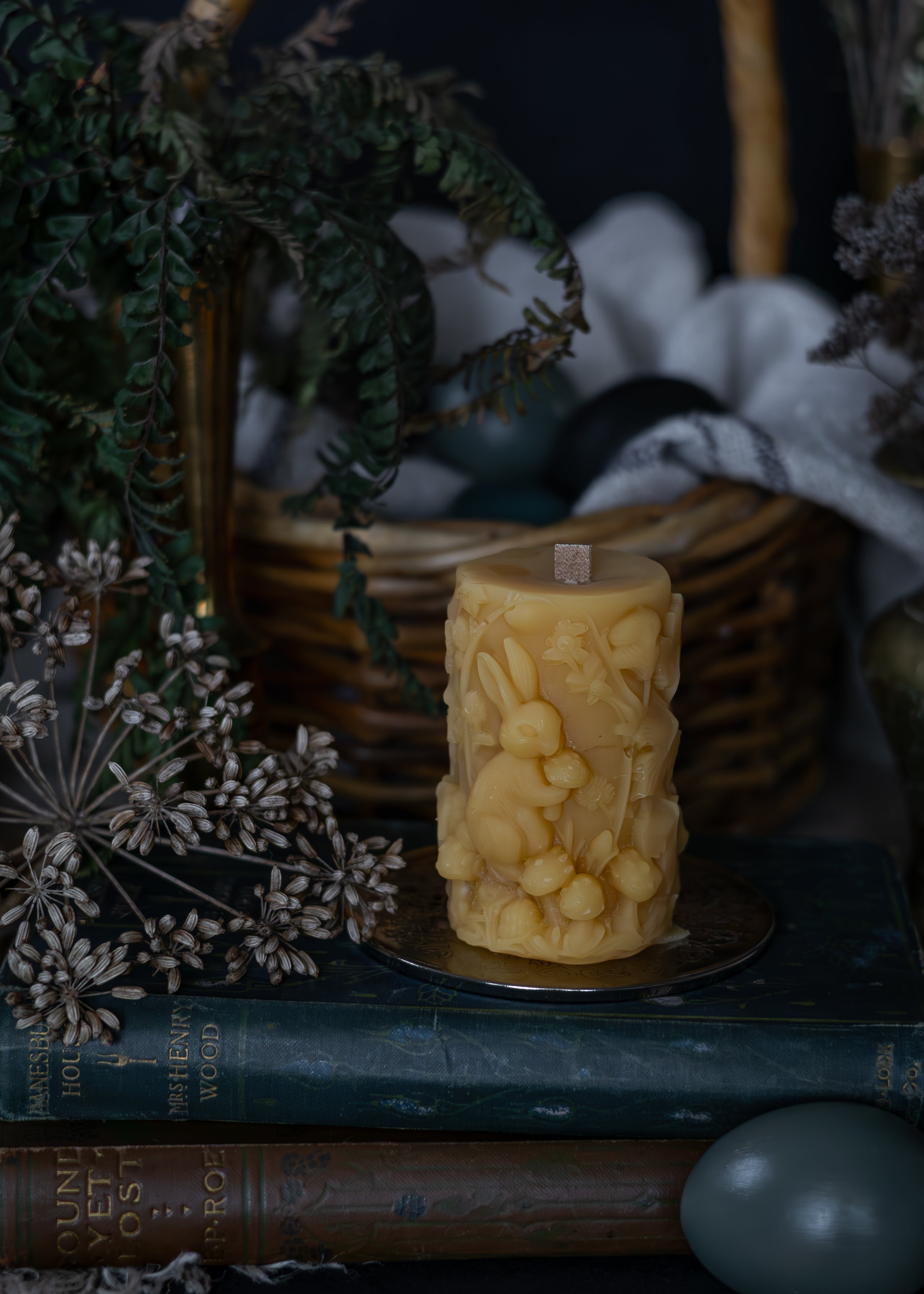 Decorative candle with intricate design on a dark surface with books and plants, tasmanian beeswax easter candle
