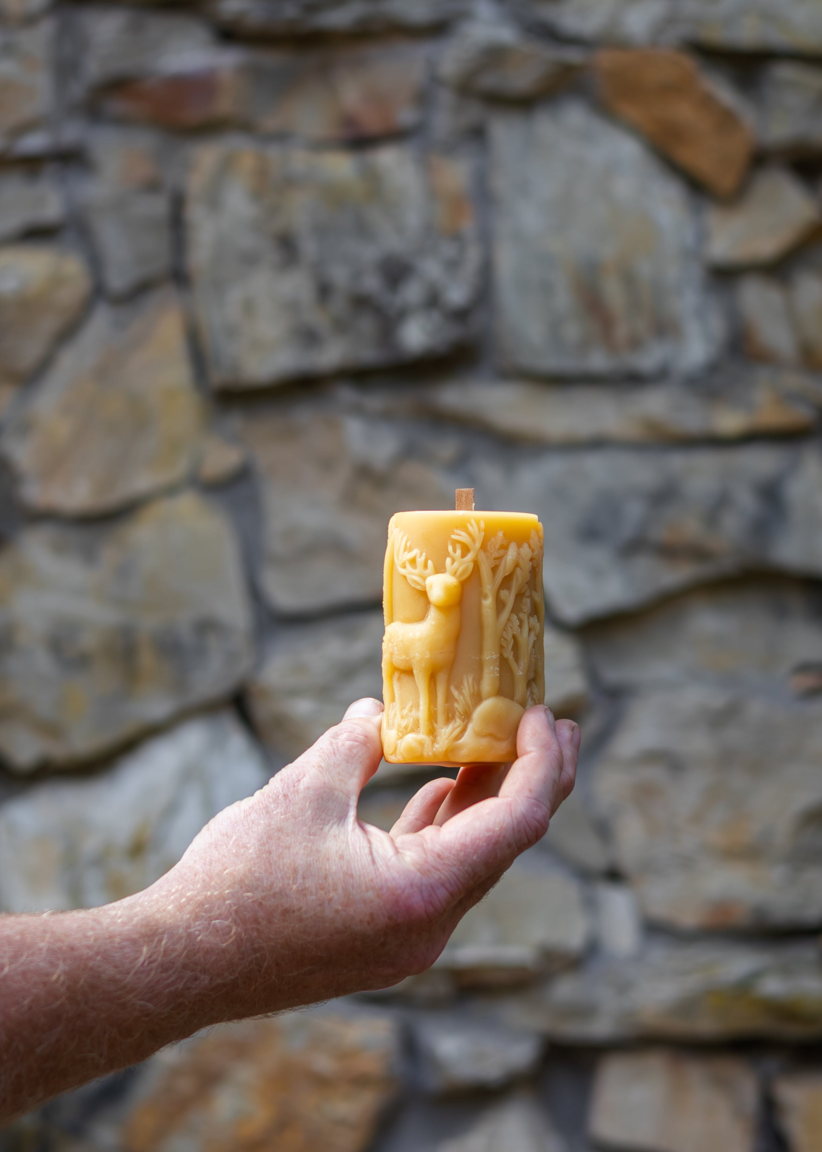 Hand holding a beeswax block with a carved design against a stone wall.