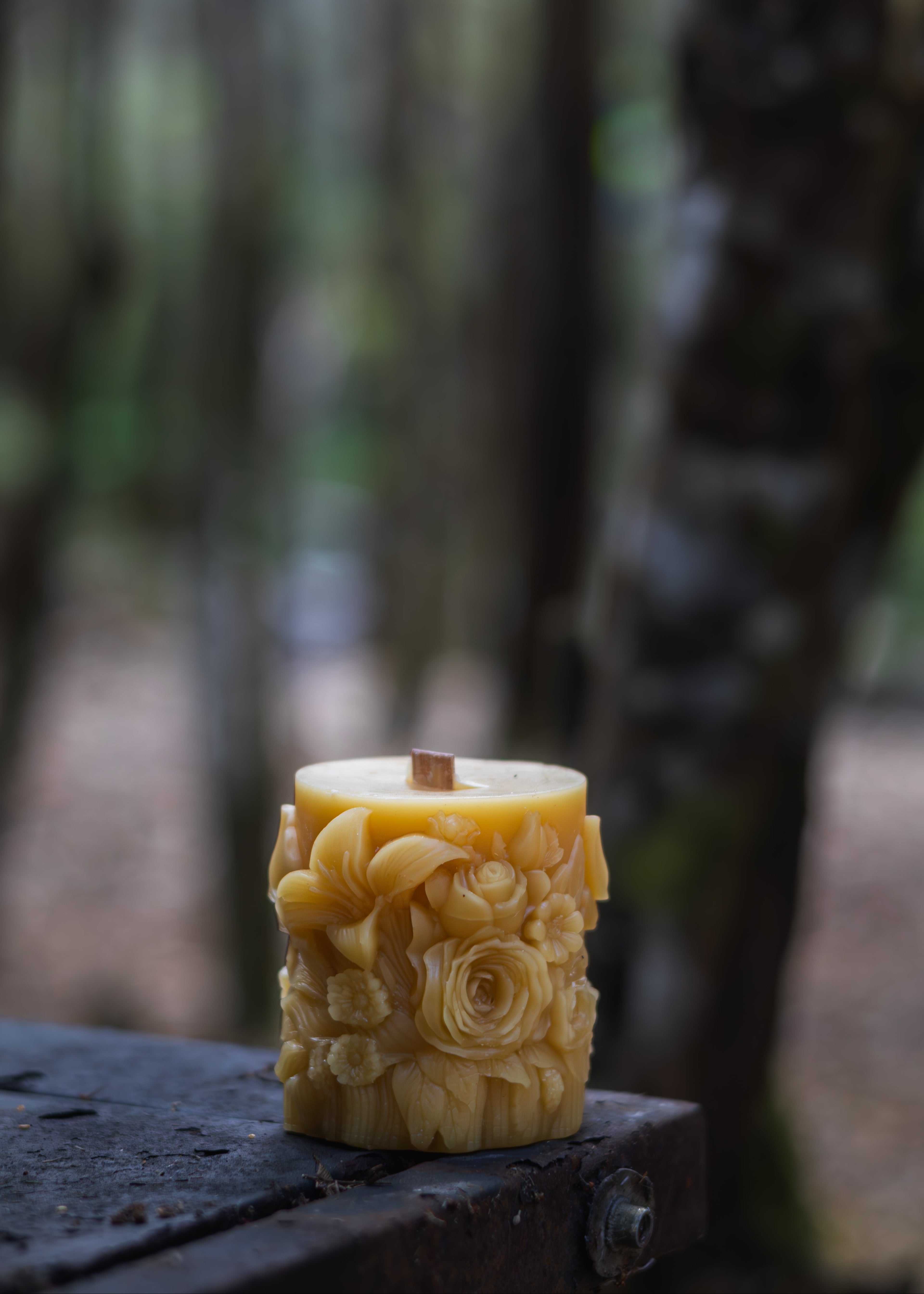 Decorative candle with floral design on a wooden surface in a forest setting