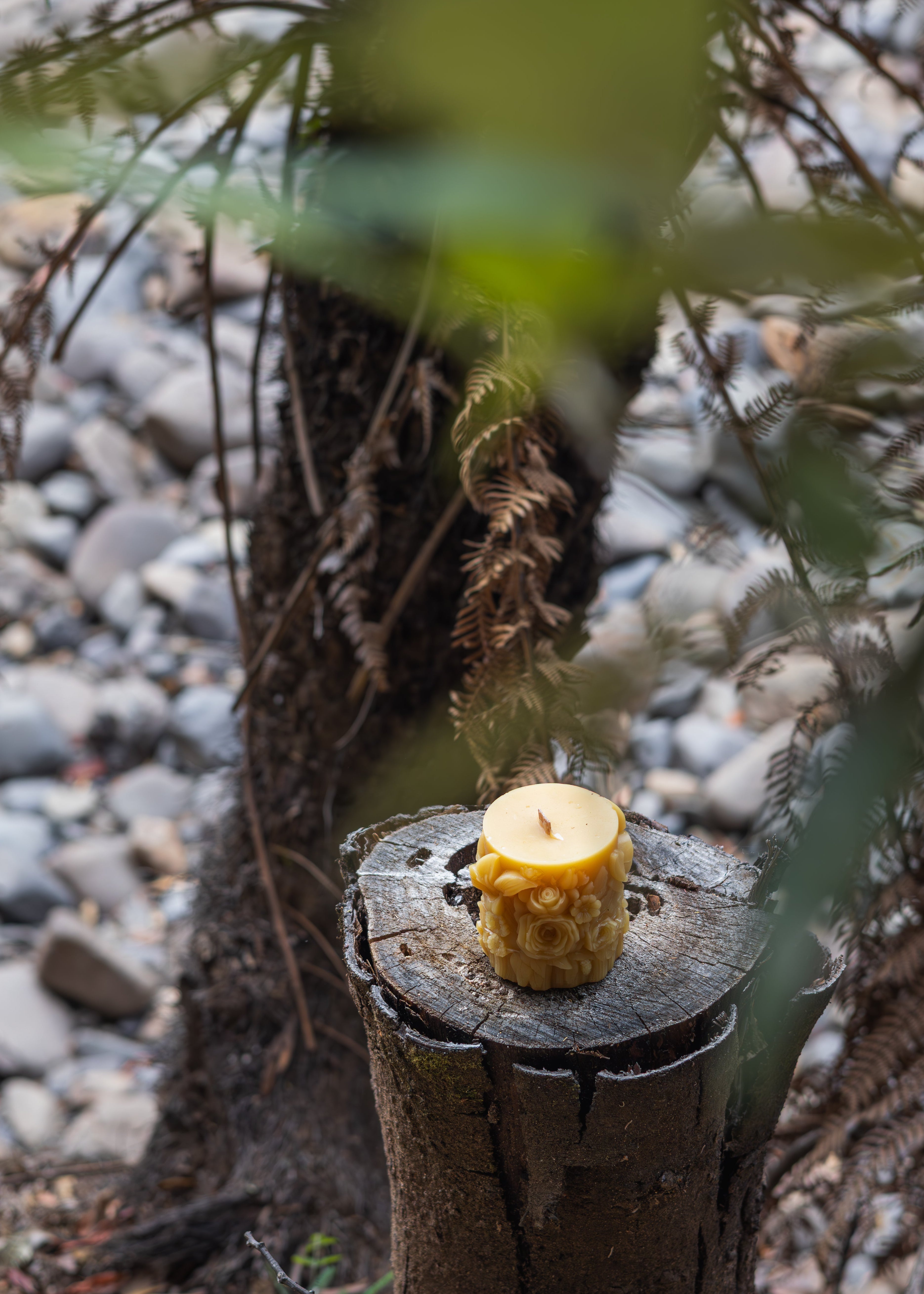 Yellow candle on a wooden stump with a natural background of rocks and plants
