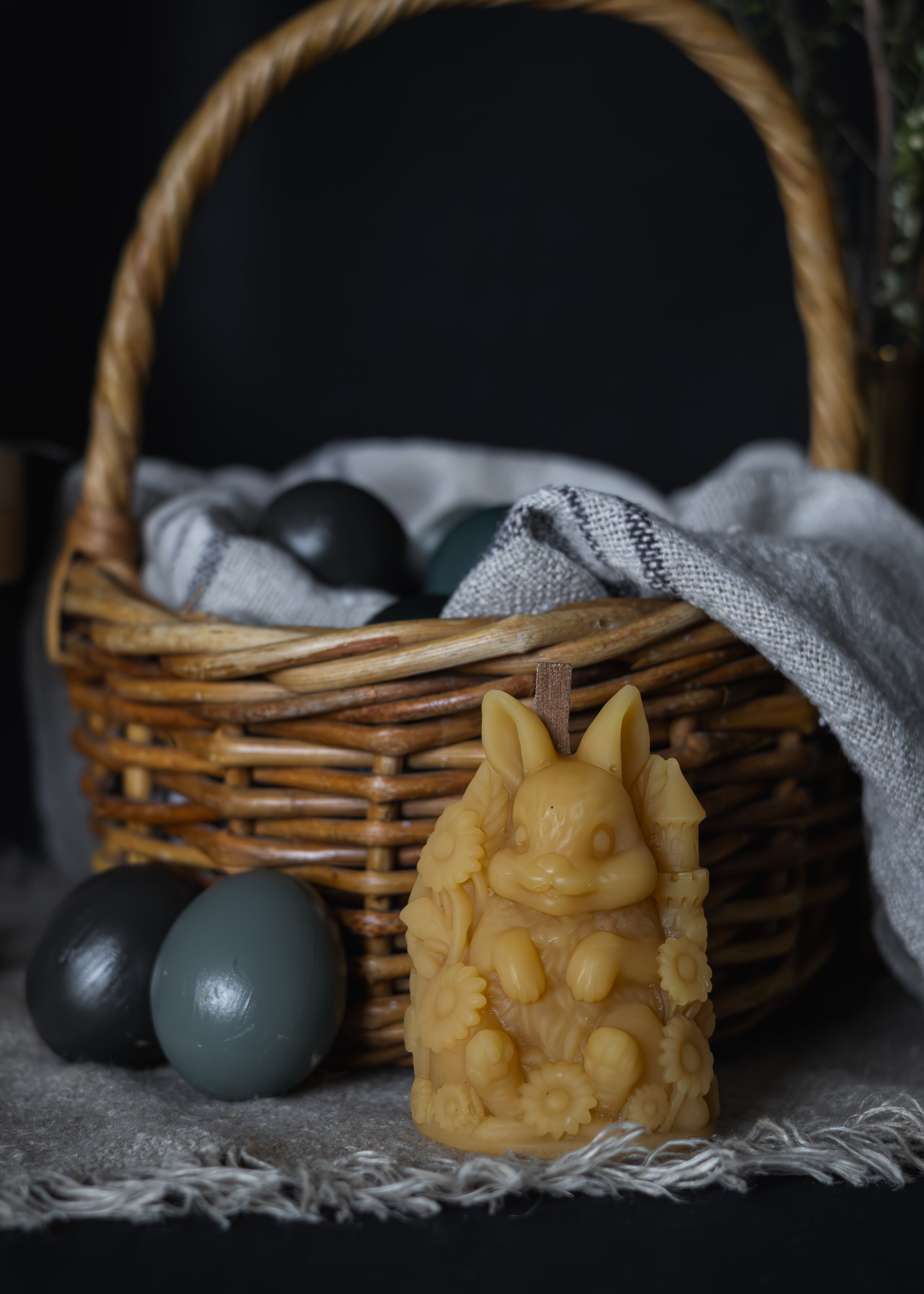Beeswax candle shaped like a rabbit with a wicker basket and stones in the background, tasmanian beeswax candle