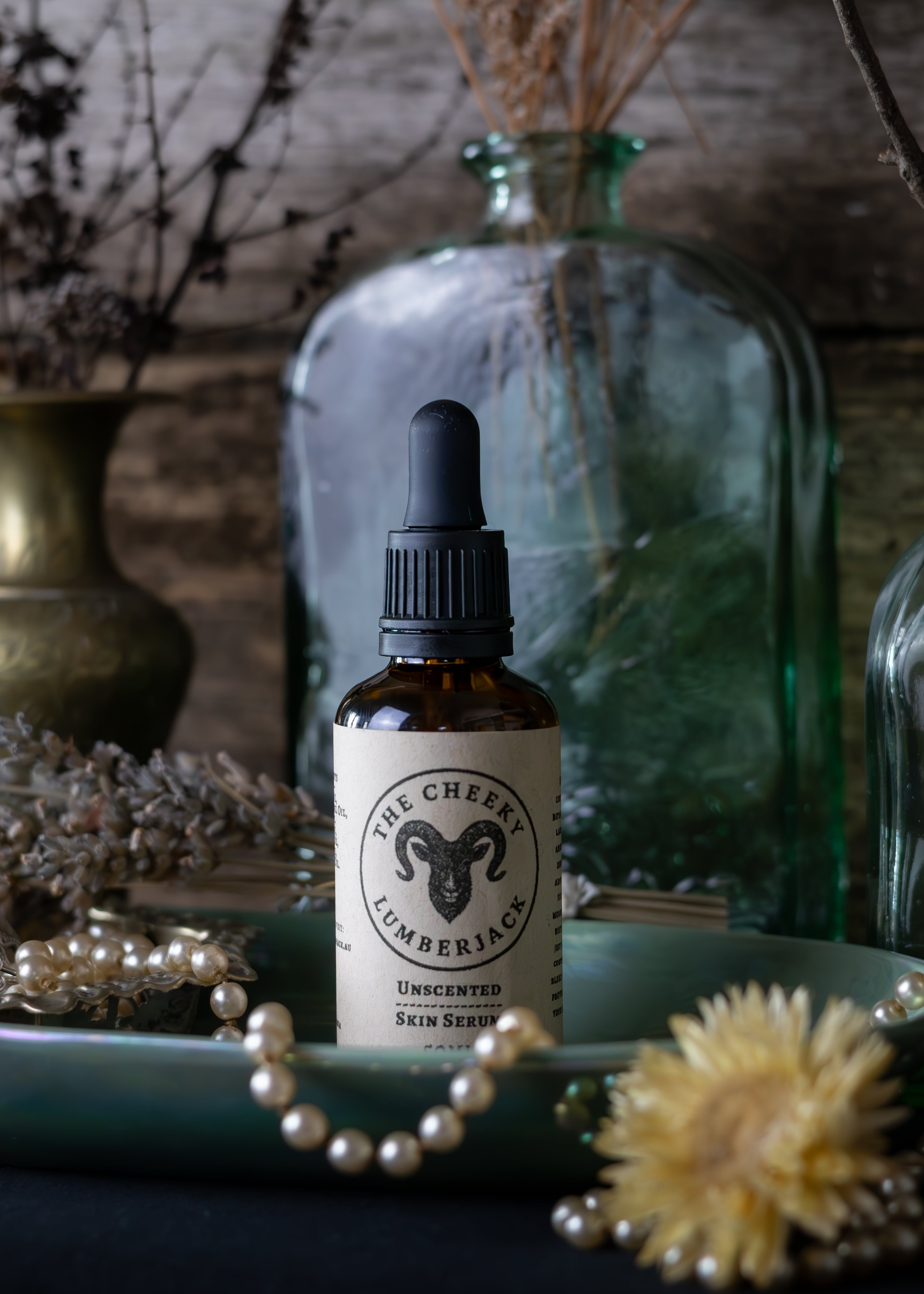 Bottle of 'The Cheeky Lumberjack' skin serum on a decorative surface with dried plants and jars.