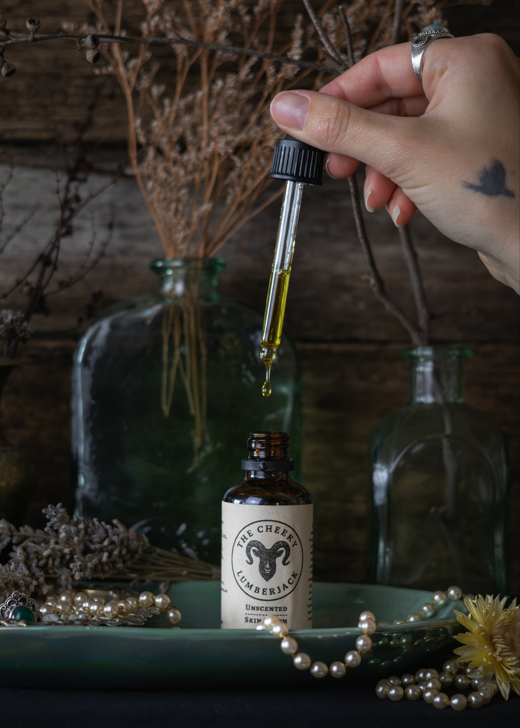 Hand holding a dropper with liquid over a bottle labeled 'The Witching Hour' amidst decorative elements.