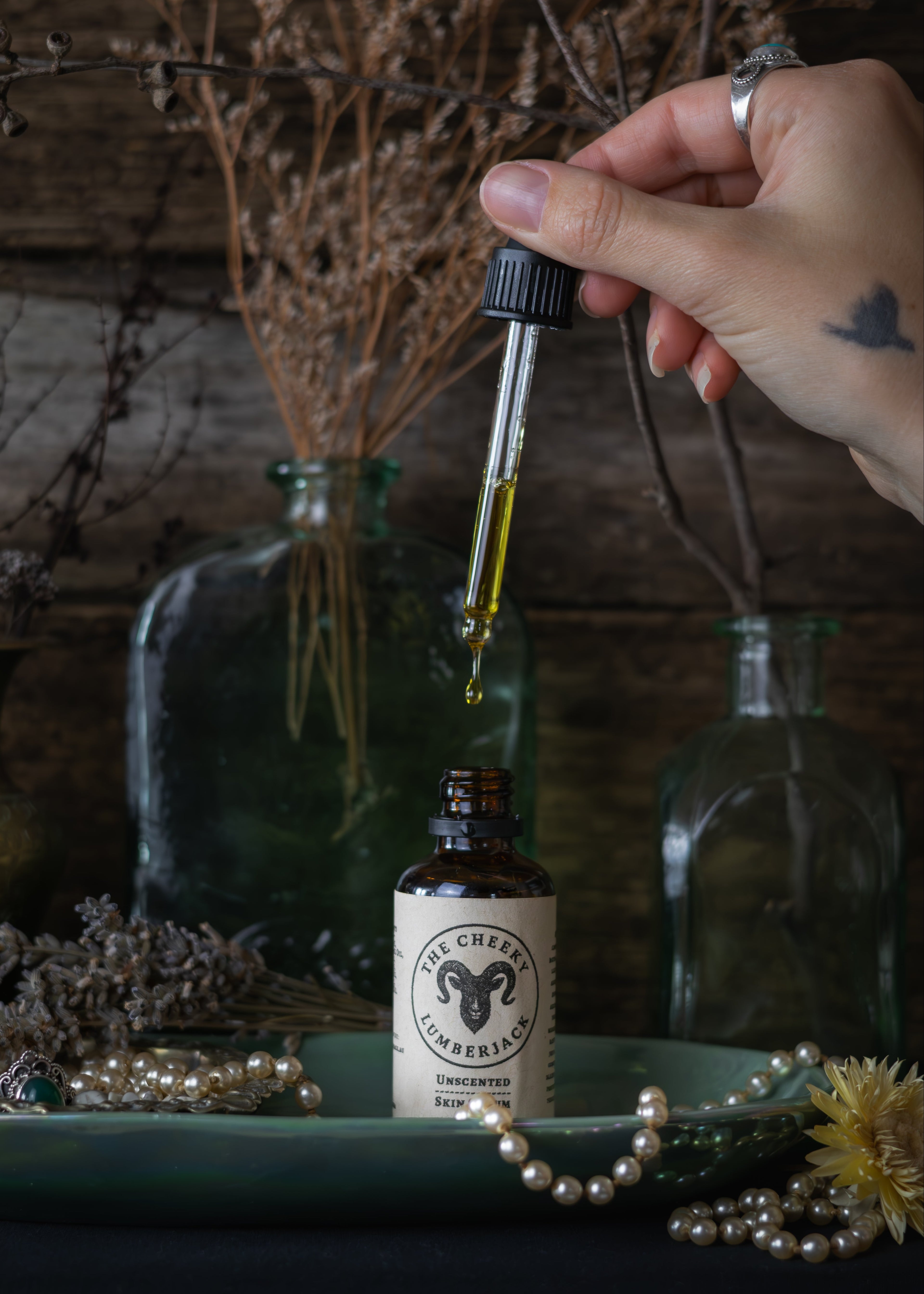 Hand holding a dropper with liquid over a bottle labeled 'The Witching Hour' amidst decorative elements.