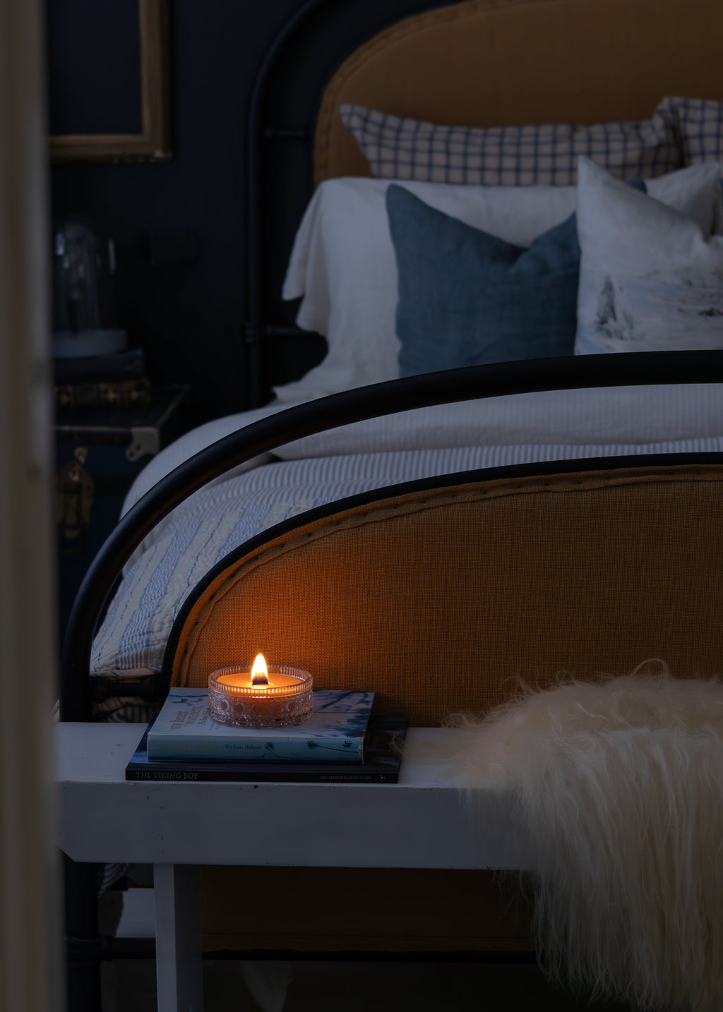Bed with pillows and a vintage crystal Tasmanian beeswax lit candle on a nightstand in a bedroom setting.