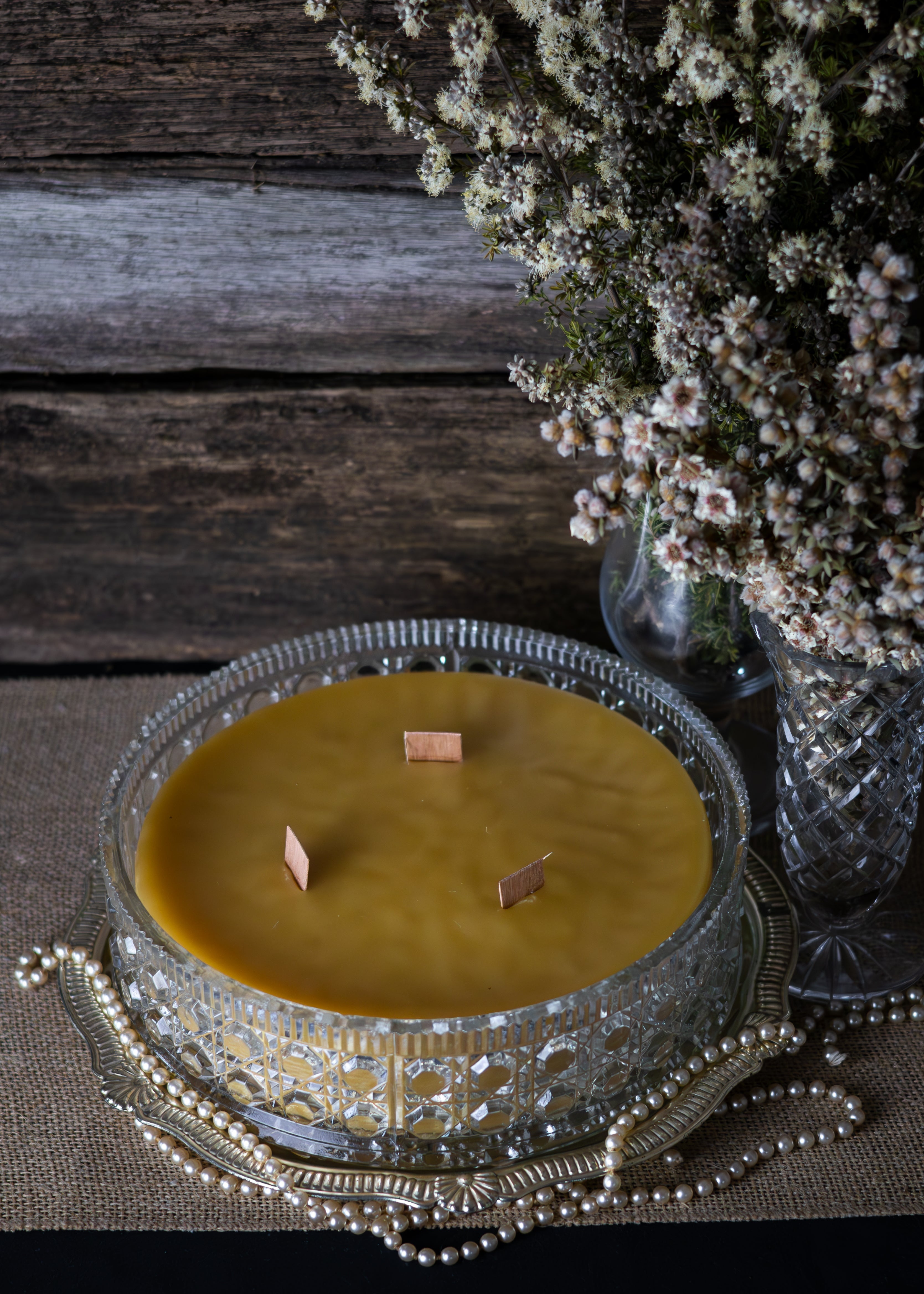 Candle in a decorative holder with a vase of flowers on a wooden surface