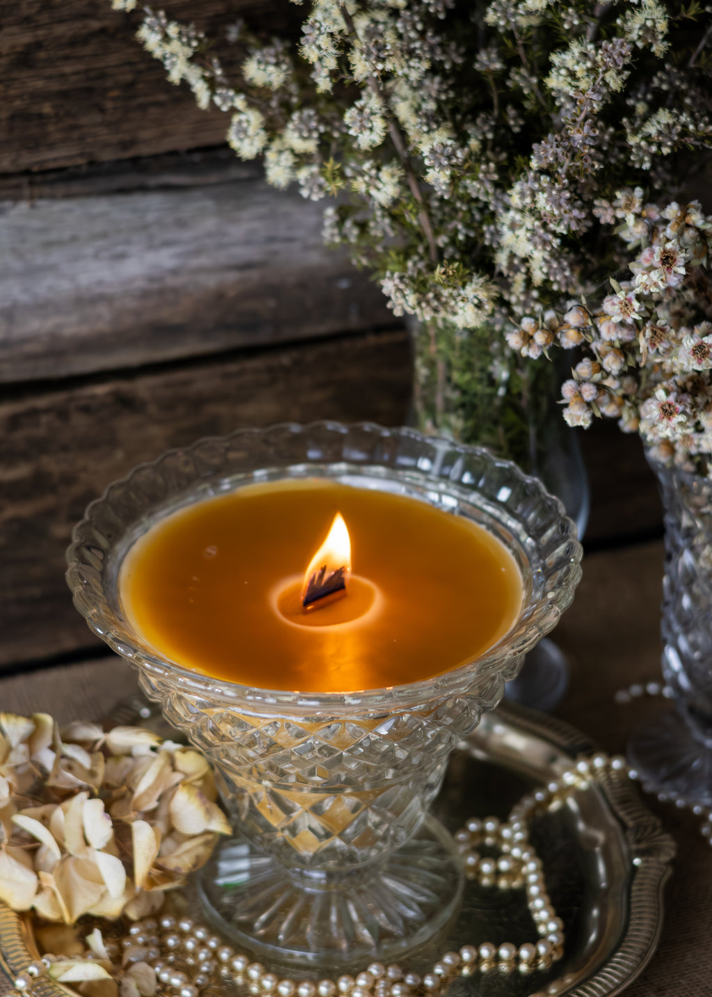 Candle in a decorative glass holder with flowers and dried elements on a wooden surface