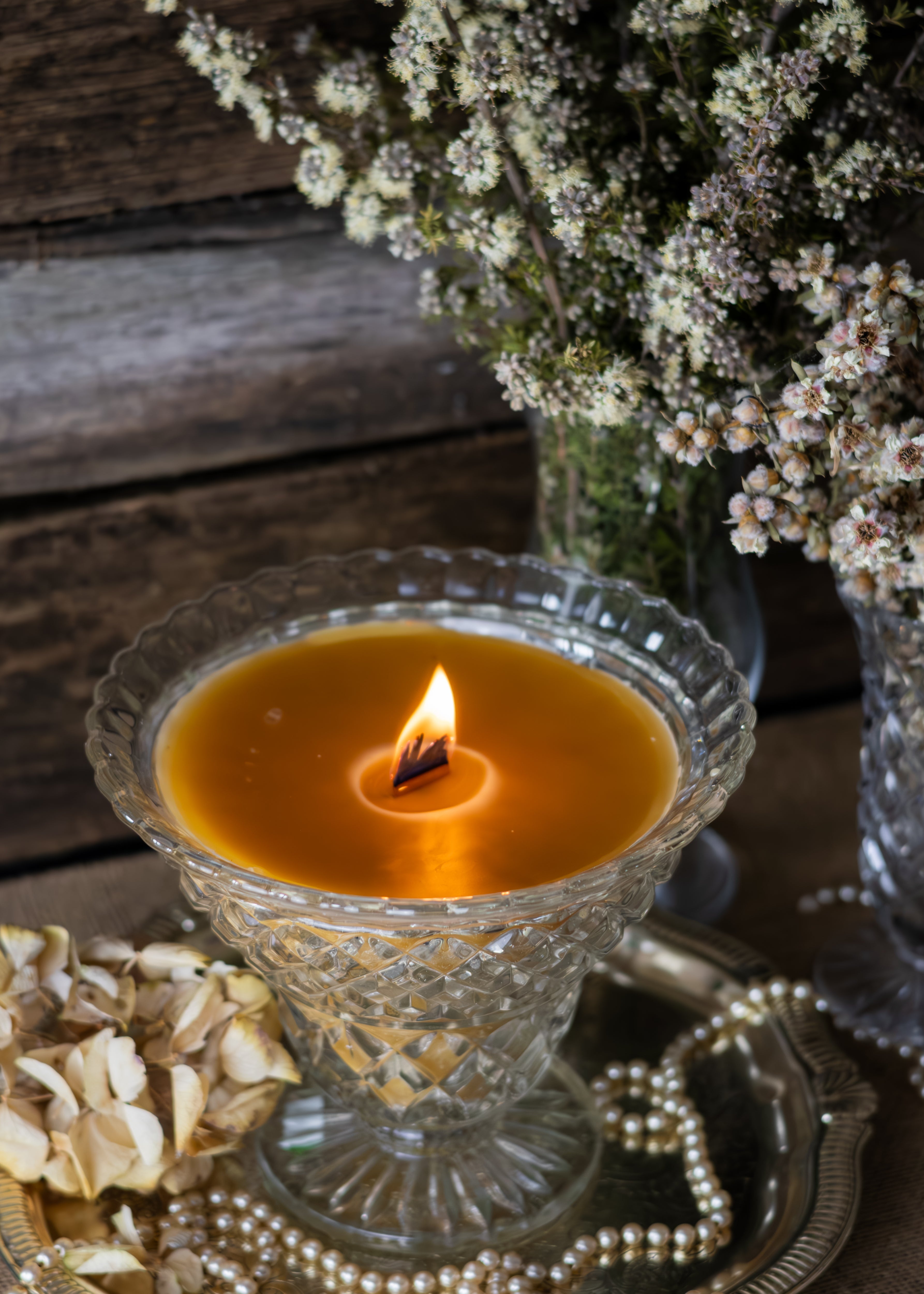 Candle in a decorative glass holder with flowers and dried elements on a wooden surface